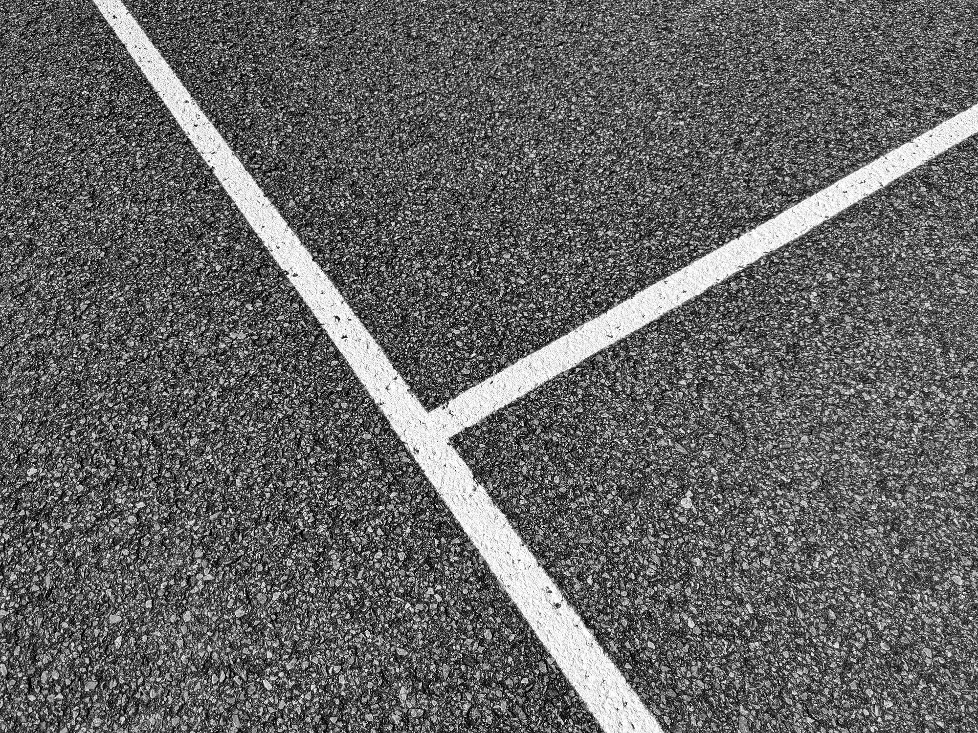 White road markings meeting at a junction on dark asphalt, a visual for tracking progress along a target trajectory