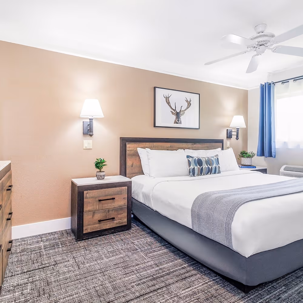 A warmer angle on the king bedroom — wood headboard, sconces, and that calming earthy palette.