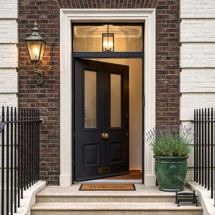 Modern brown vertical panel front door with side glass panels framed by white brick walls and marble floor.