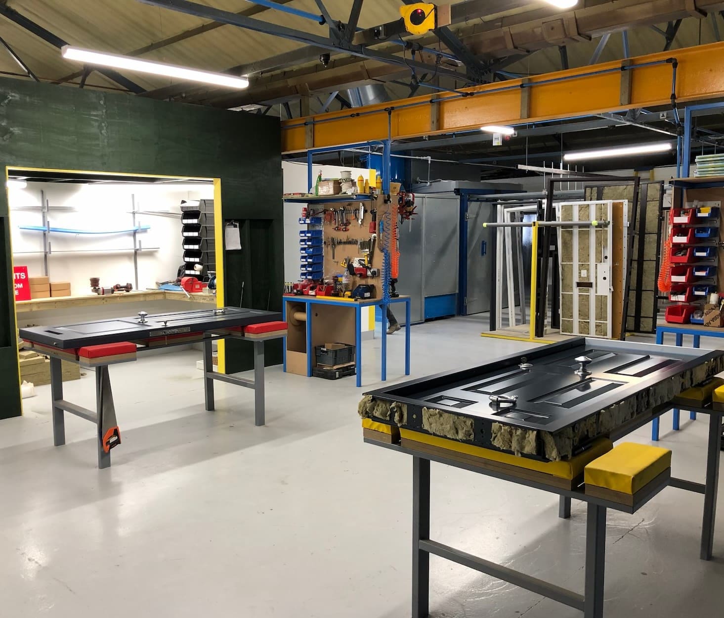 Indoor workshop space with two black doors on worktables, tool station, and metal shelves under AXIS sign.