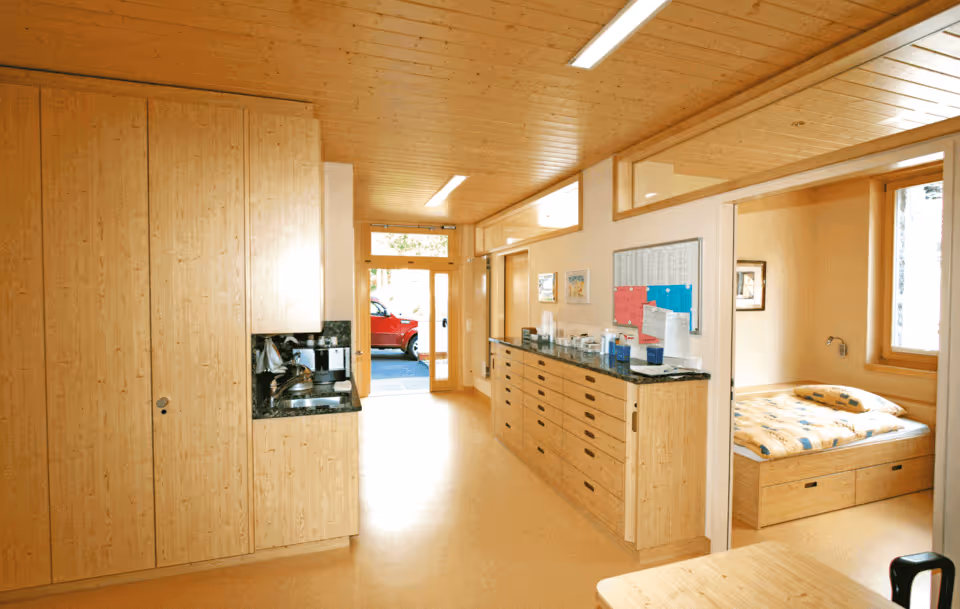 Bright hallway with wooden cabinets, ceiling, and floor, leading to an adjacent room with a bed.