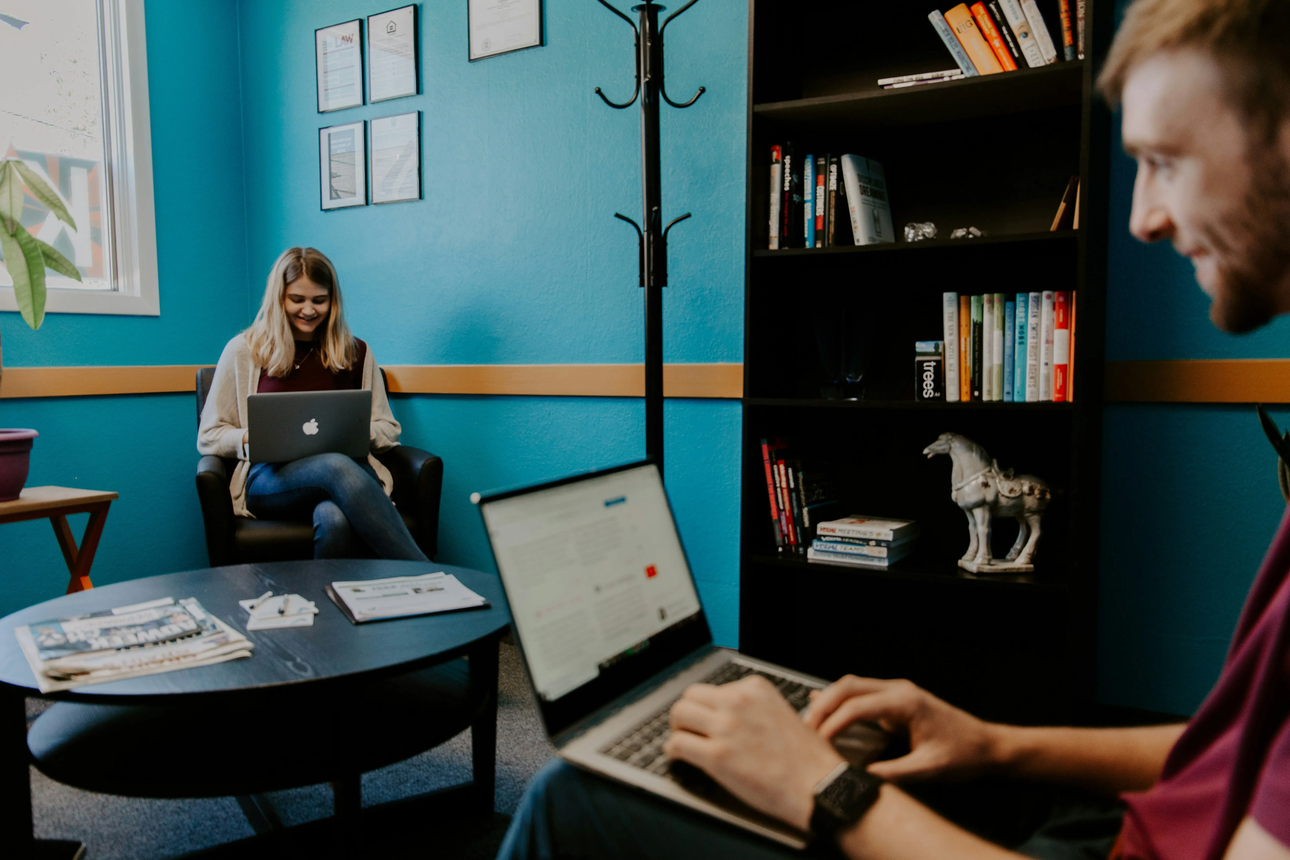A man and a woman sitting in a room with laptops.