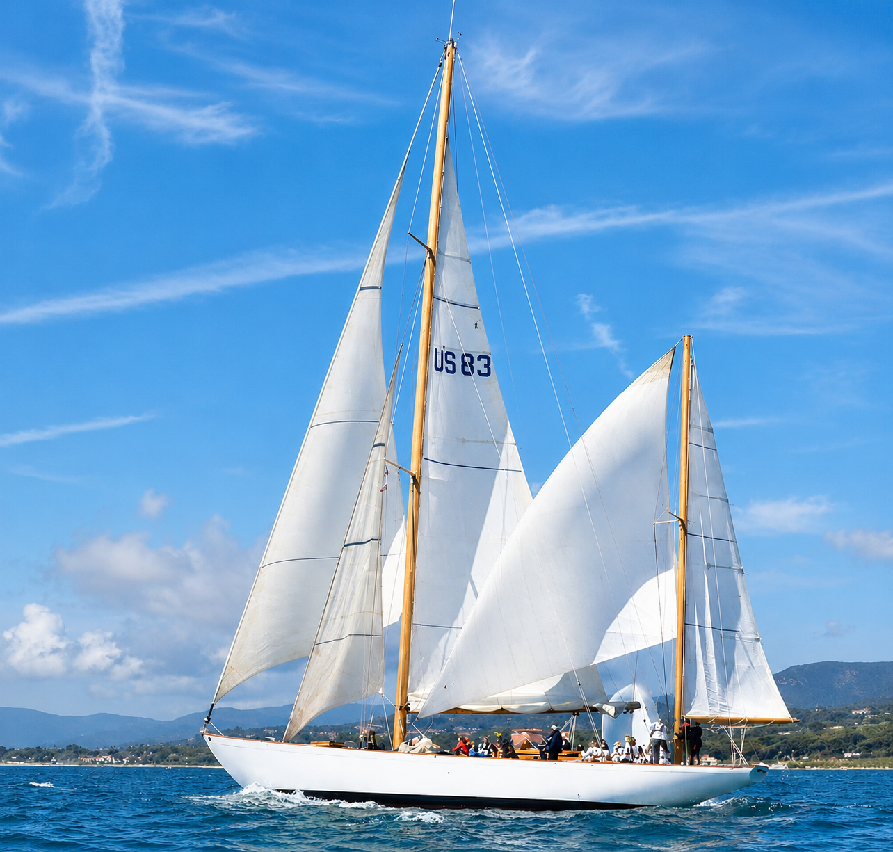 Grand voilier blanc avec plusieurs voiles gonflées naviguant sur une mer bleue sous un ciel dégagé.