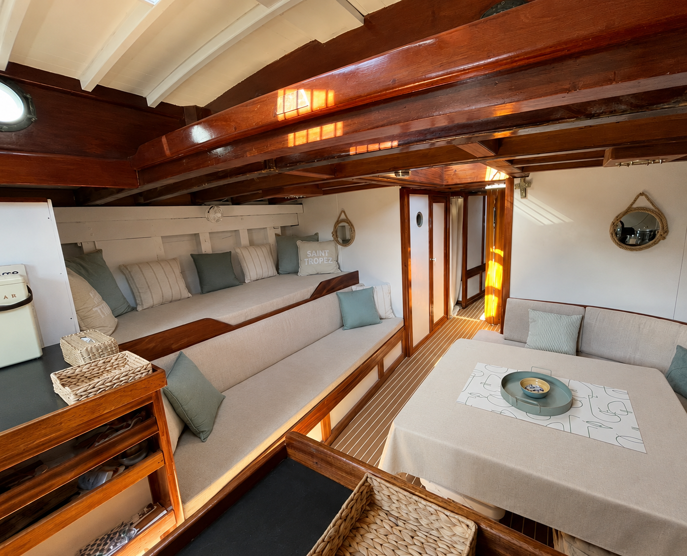 Intérieur de cabine de bateau en bois avec banquettes beiges, coussins verts et table centrée.