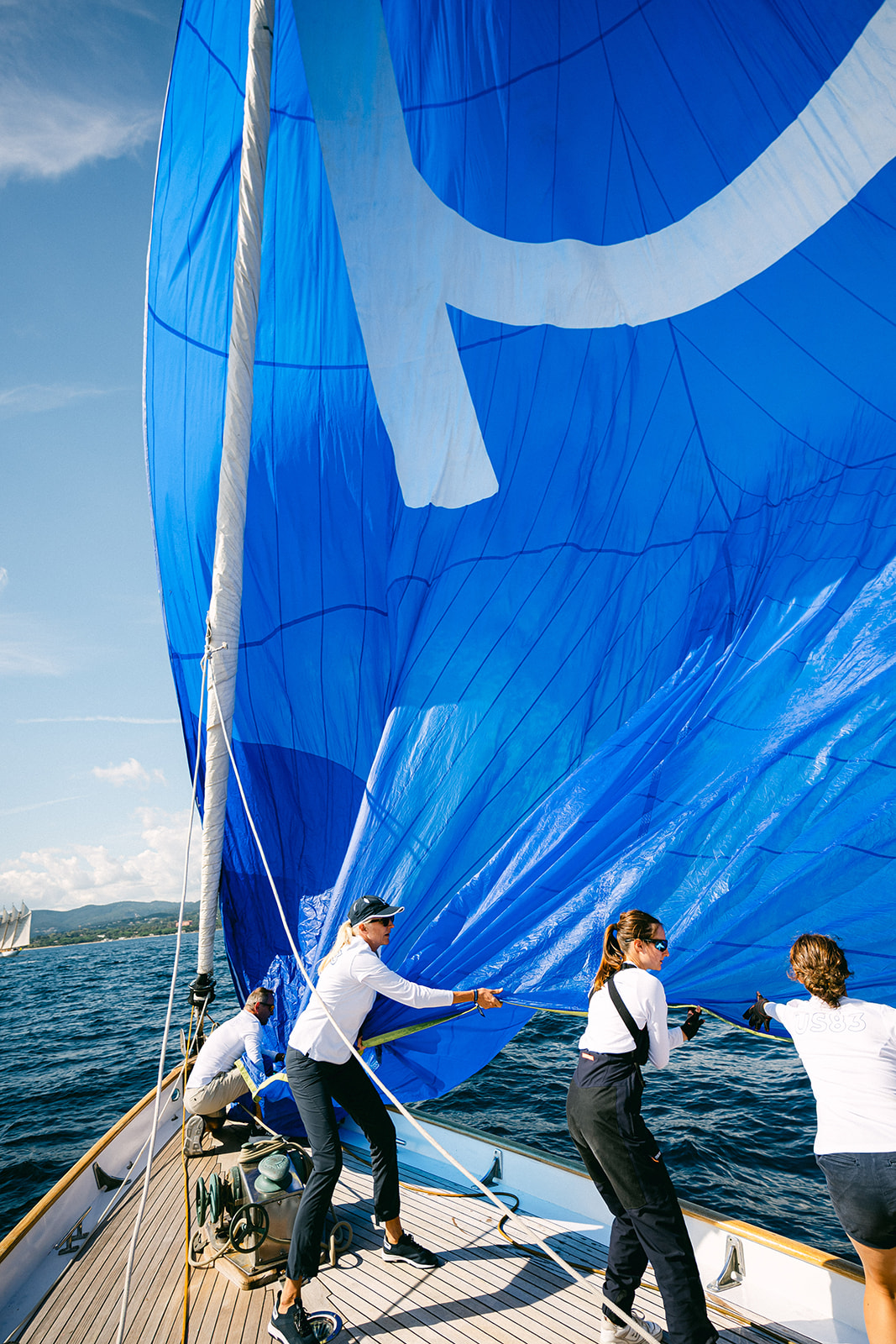 Équipage d'une voile bleue sur un voilier, tirant la voile en pleine régate en mer.