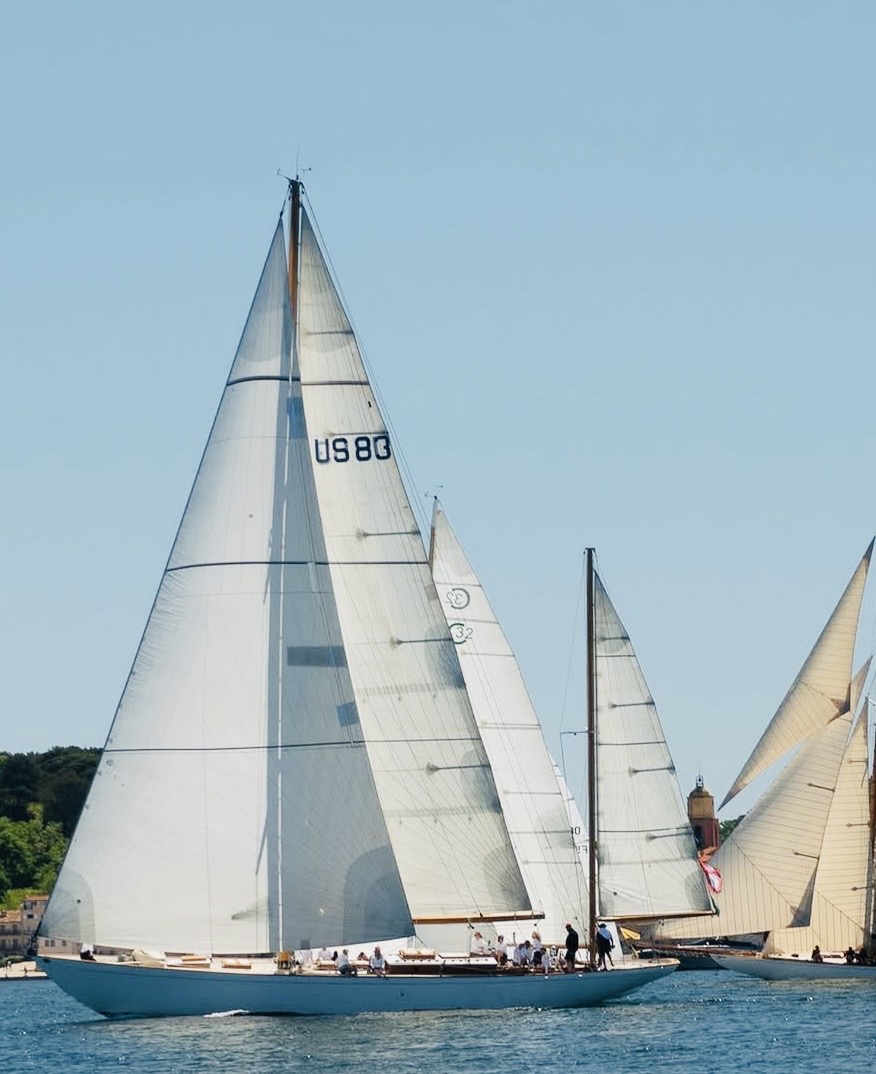 Voiliers de course sur l'eau sous un ciel bleu clair, avec des équipages à bord.