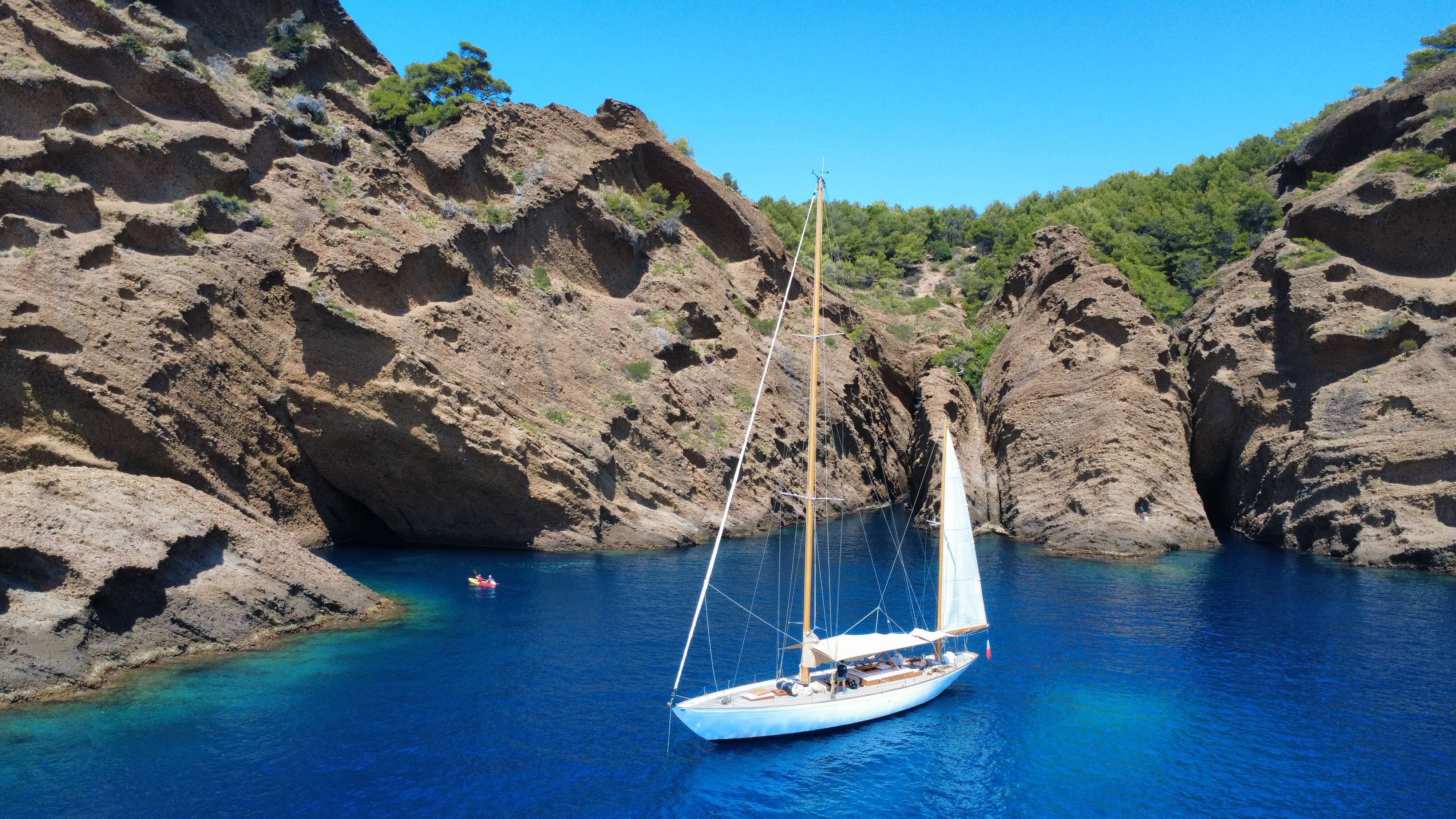 Voilier blanc ancré dans une crique entourée de hautes falaises rocheuses et d'eau bleu profond.