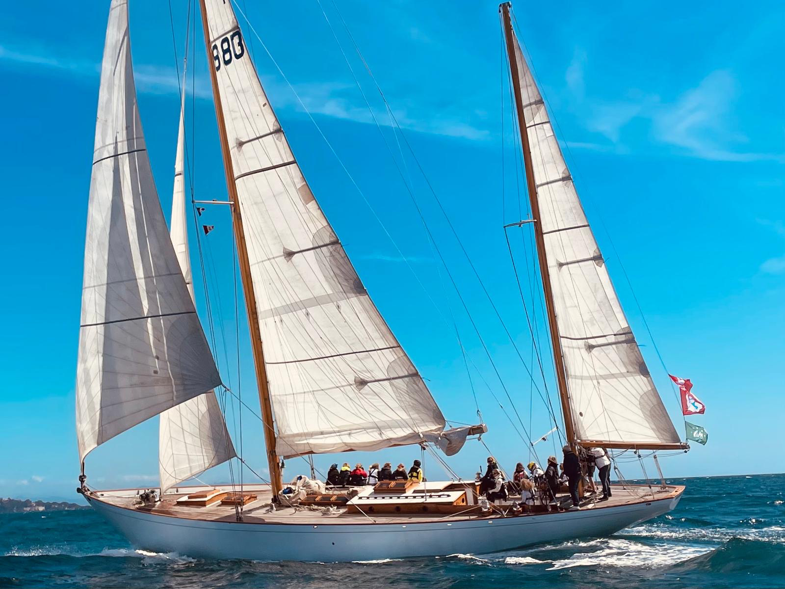 Voilier classique avec de grandes voiles blanches naviguant sur une mer bleue par temps clair.