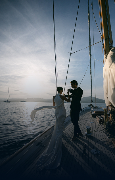 Un couple habillé pour un mariage danse sur le pont d'un voilier au coucher du soleil sur la mer.