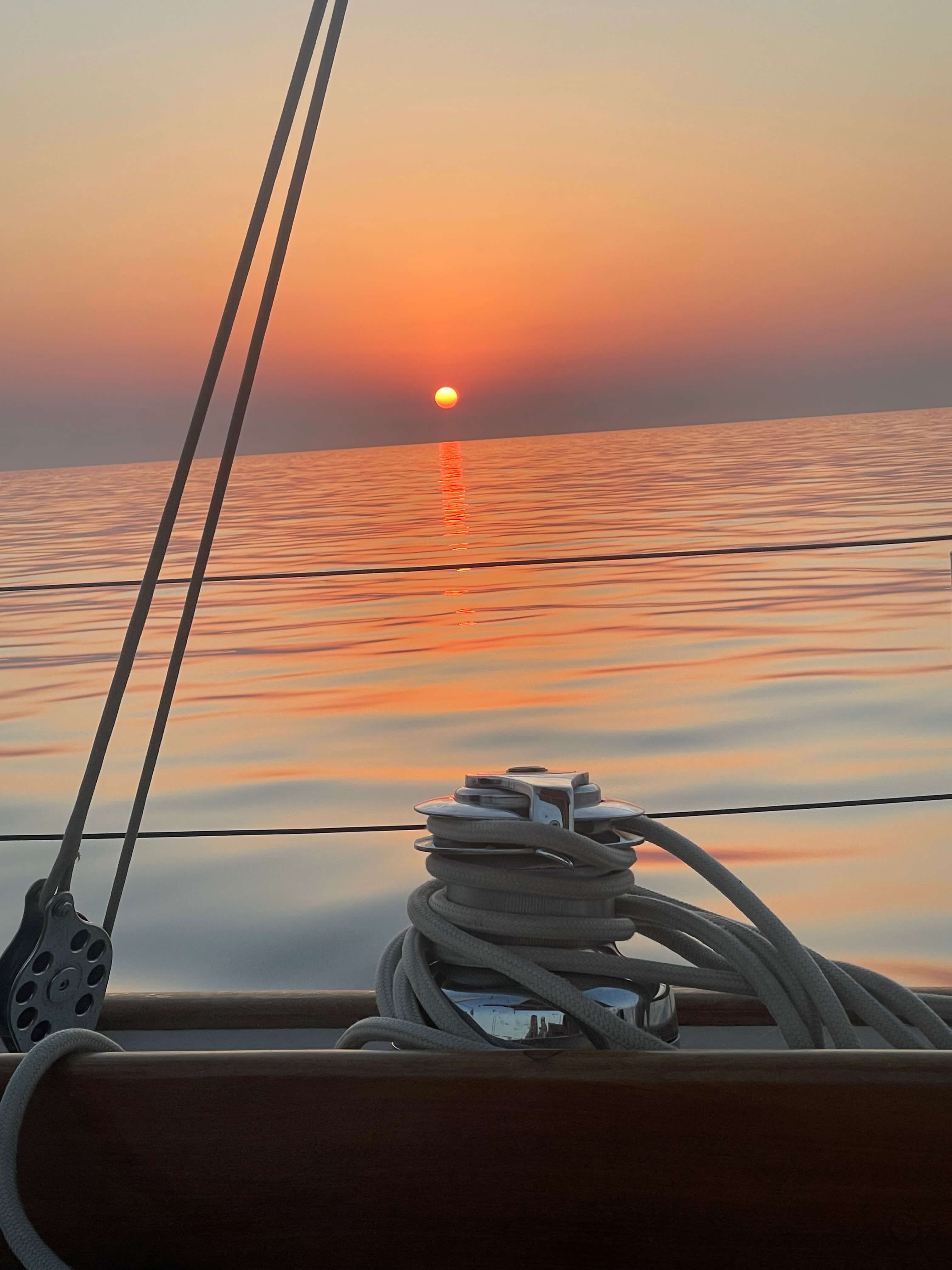 Coucher de soleil orange sur une mer calme vu depuis un voilier avec cordages.