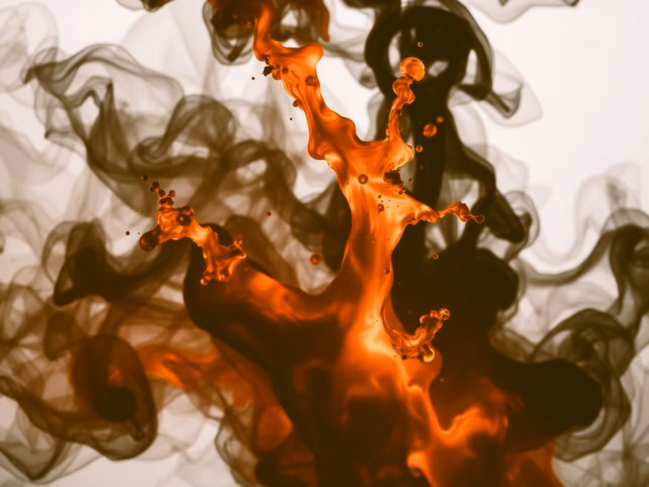 Swirling mix of translucent orange and black liquids creating abstract shapes.