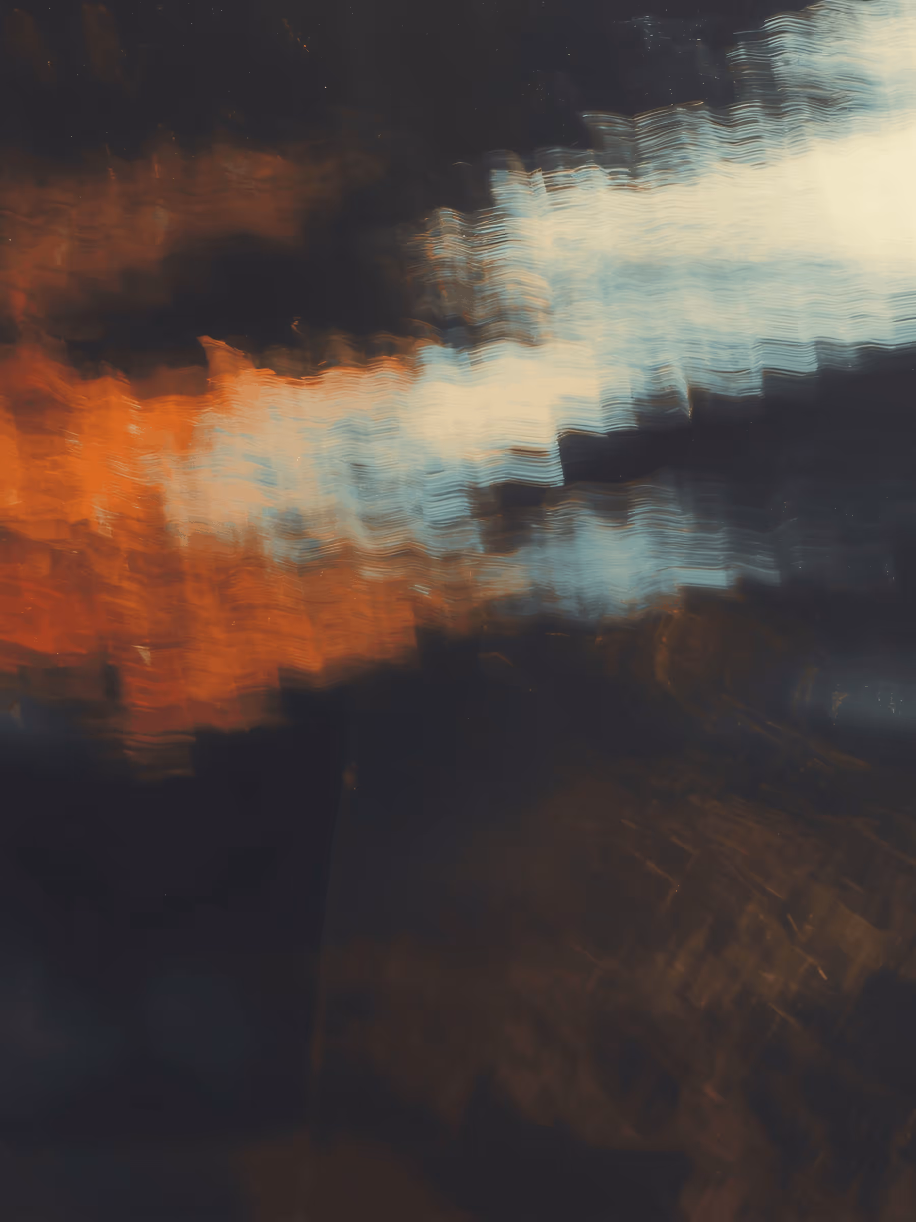 Abstract blurred image with streaks of orange, white, and blue light on a dark background.