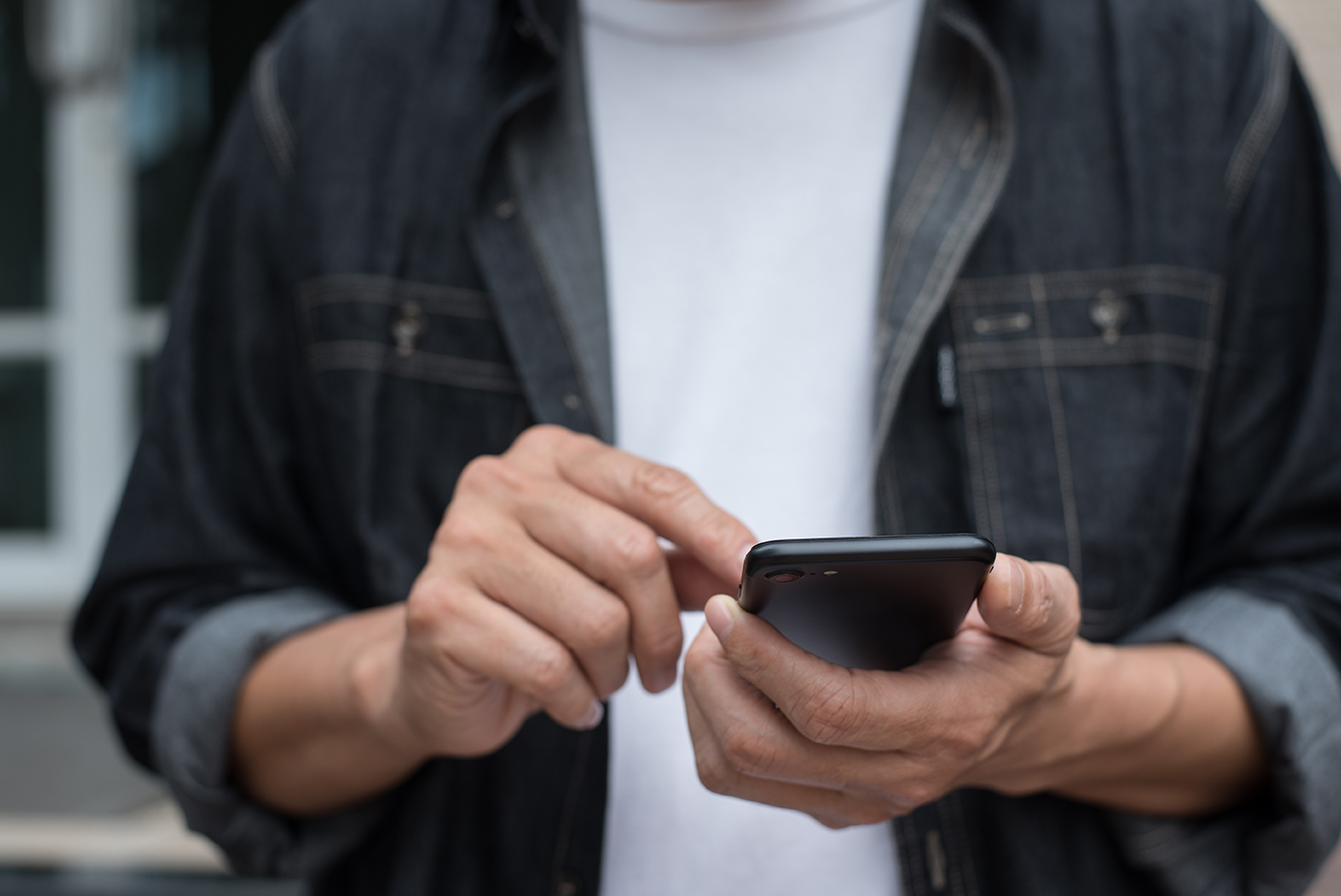 Eine Person hält und bedient ein schwarzes Smartphone mit beiden Händen.
