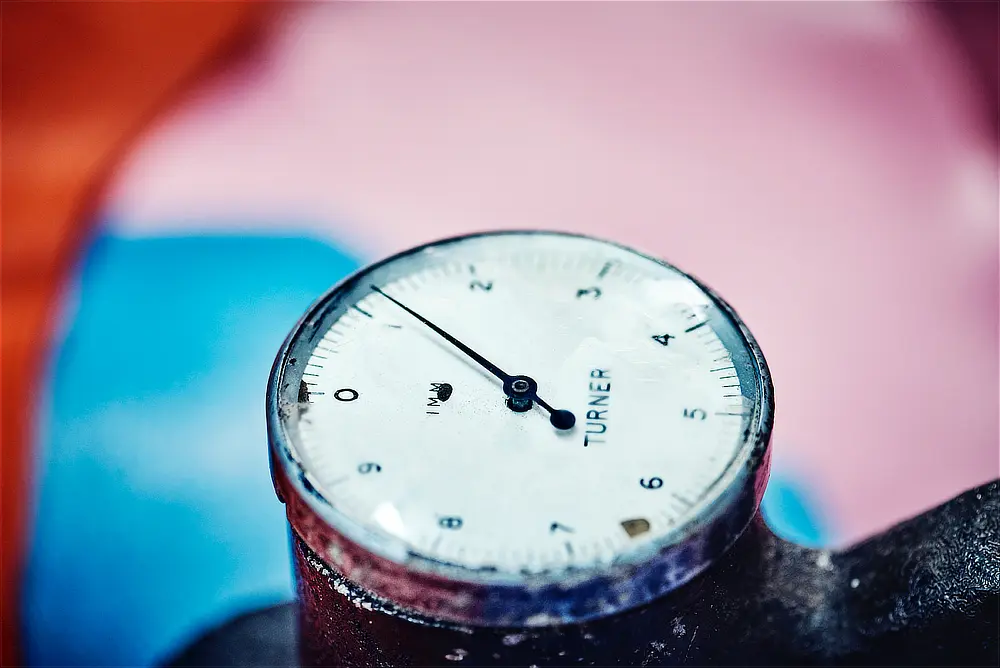 Close up of the dial of a leather thickness measuring gauge with brightly coloured goat skin in the background