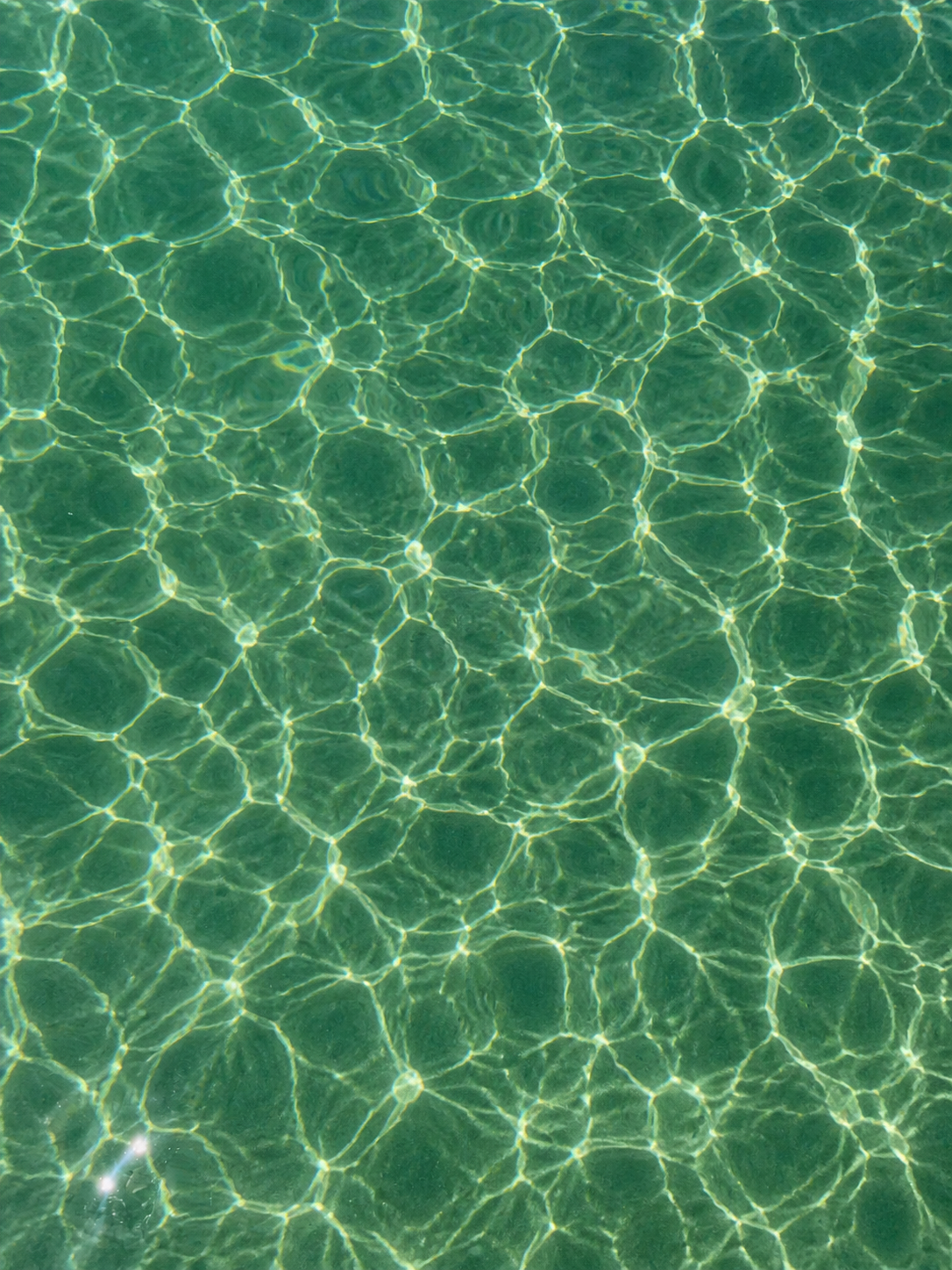 Sunlight reflecting on clear green water creating a pattern of light ripples.