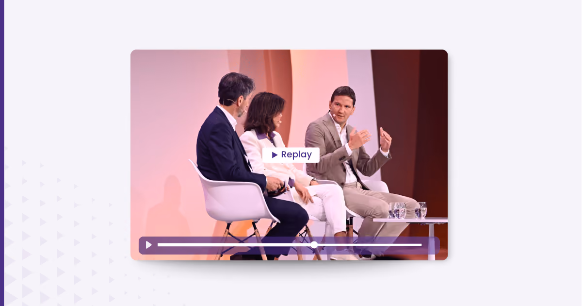 Three people seated on stage in a panel discussion with replay button overlay and water glasses on table.