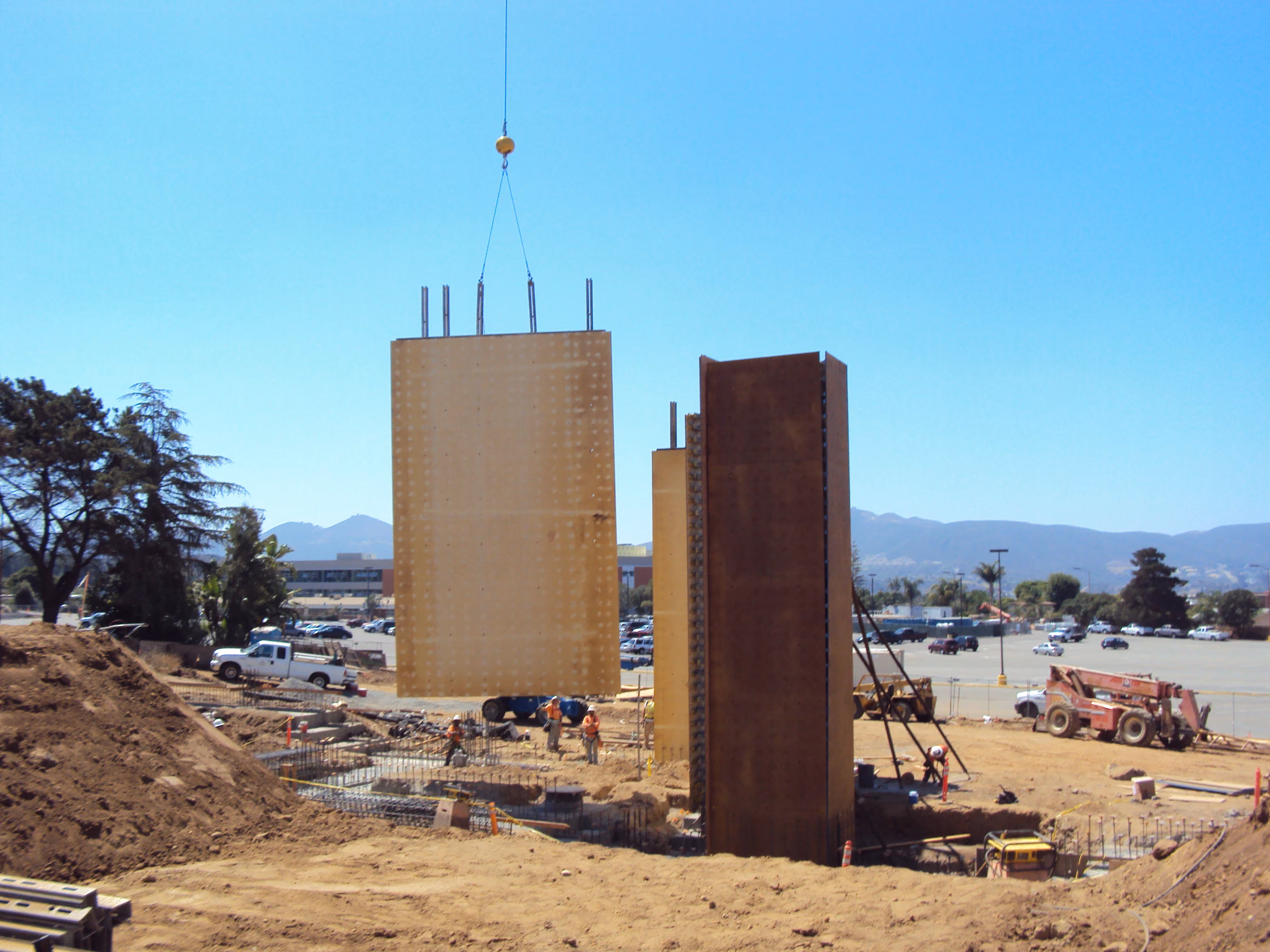 Construction crew guiding a large wall-form panel into position by crane