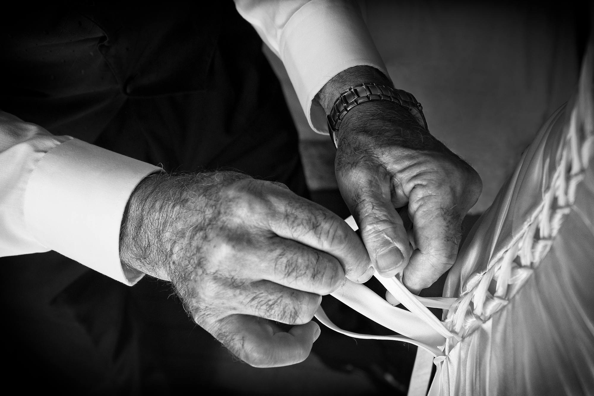 Father of the bride lacing up the back of her wedding dress, black and white detail