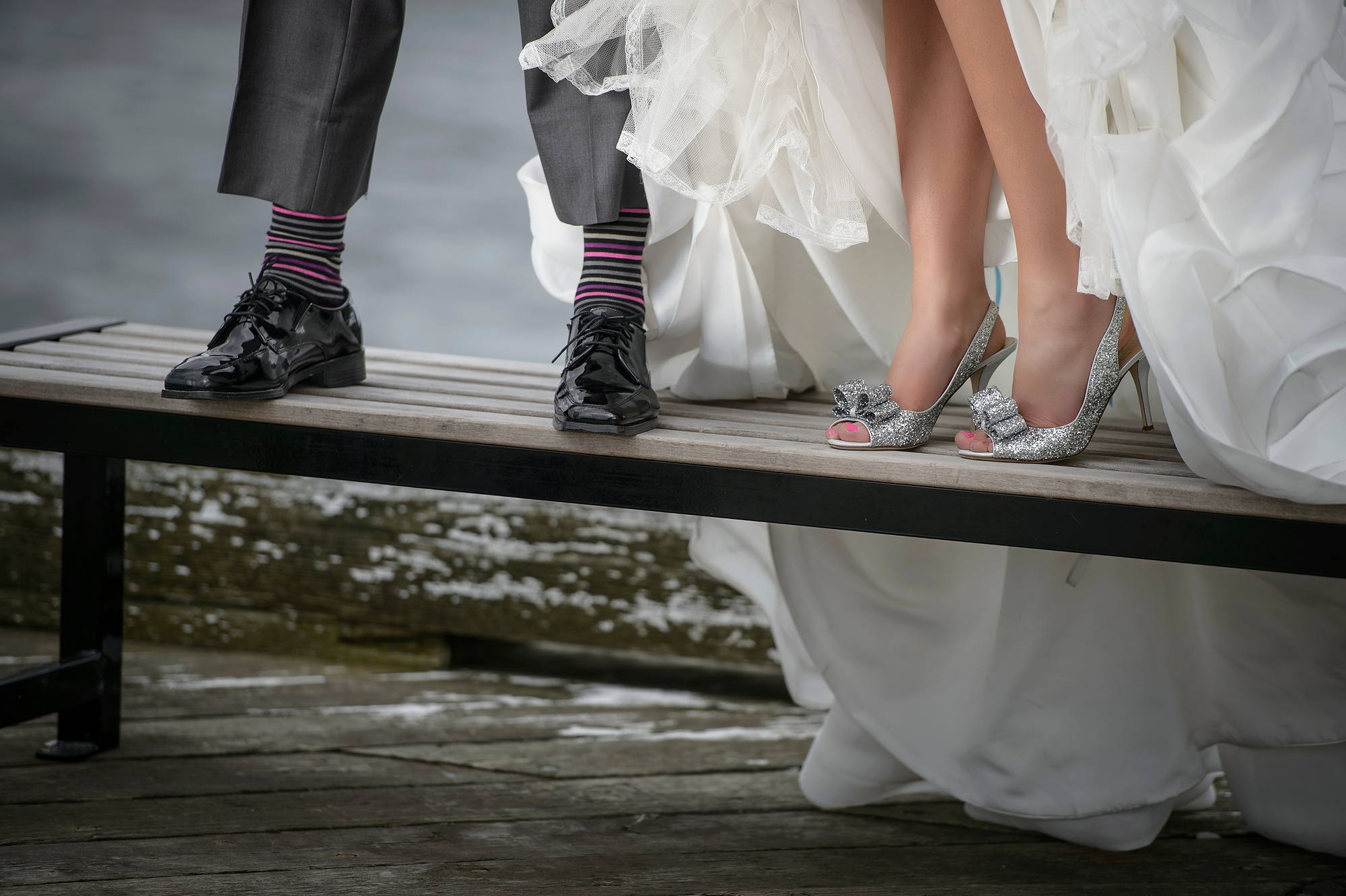 Groom's striped socks and bride's sparkly heels on a bench by the water, wedding detail