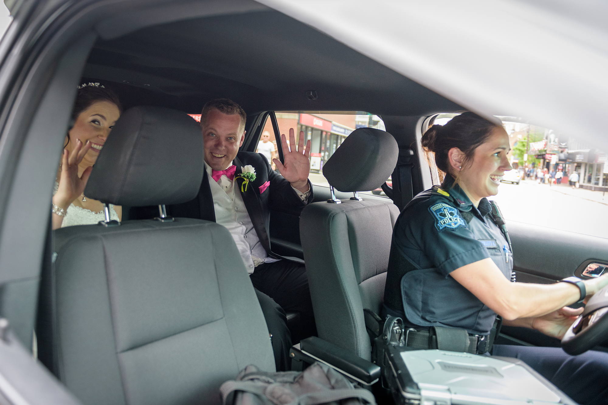 Bride and groom waving from the back seat of a police car after their Halifax wedding