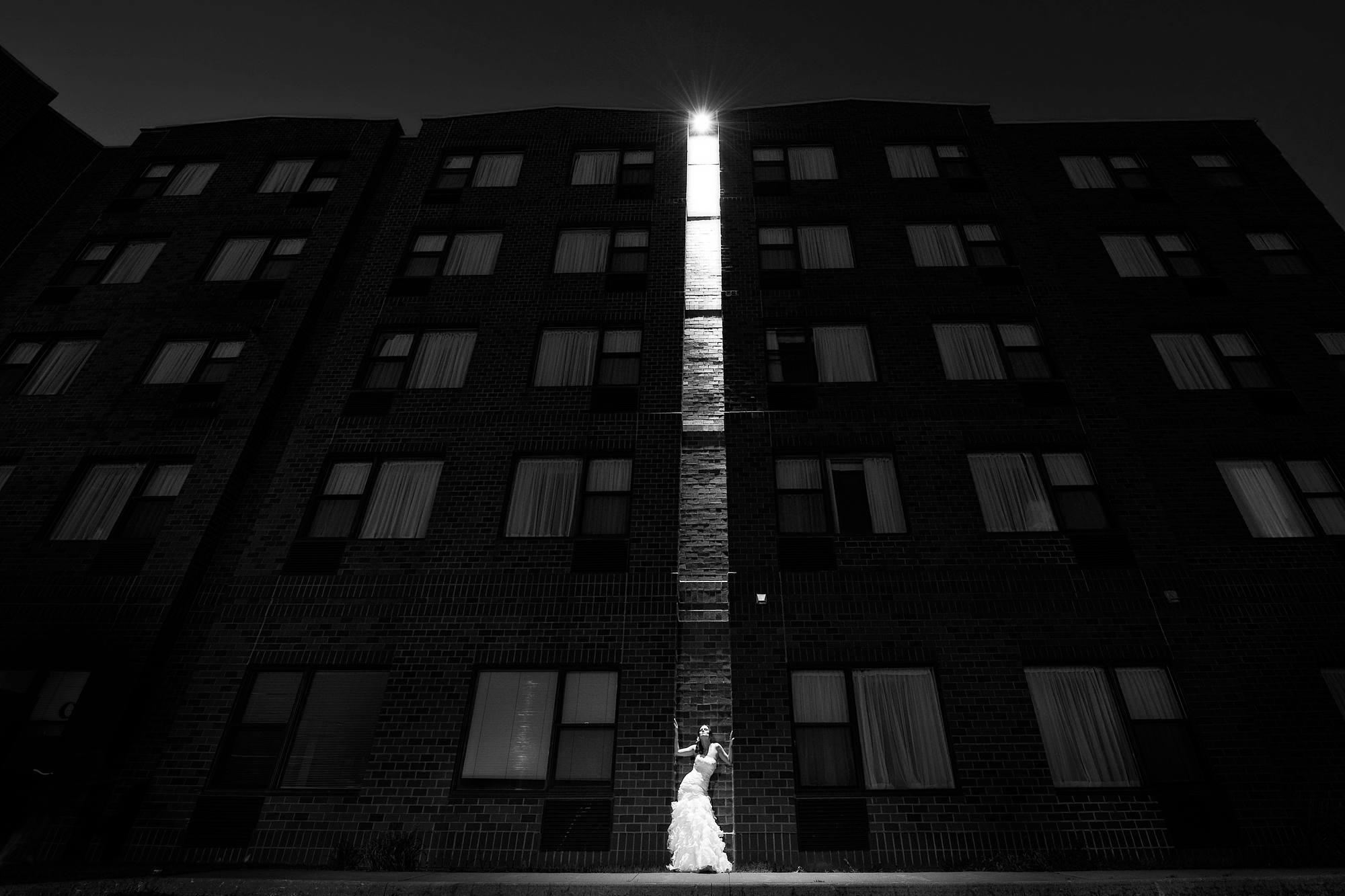 Bride lit by a single stairwell window against the Delta Dartmouth hotel at night, black and white