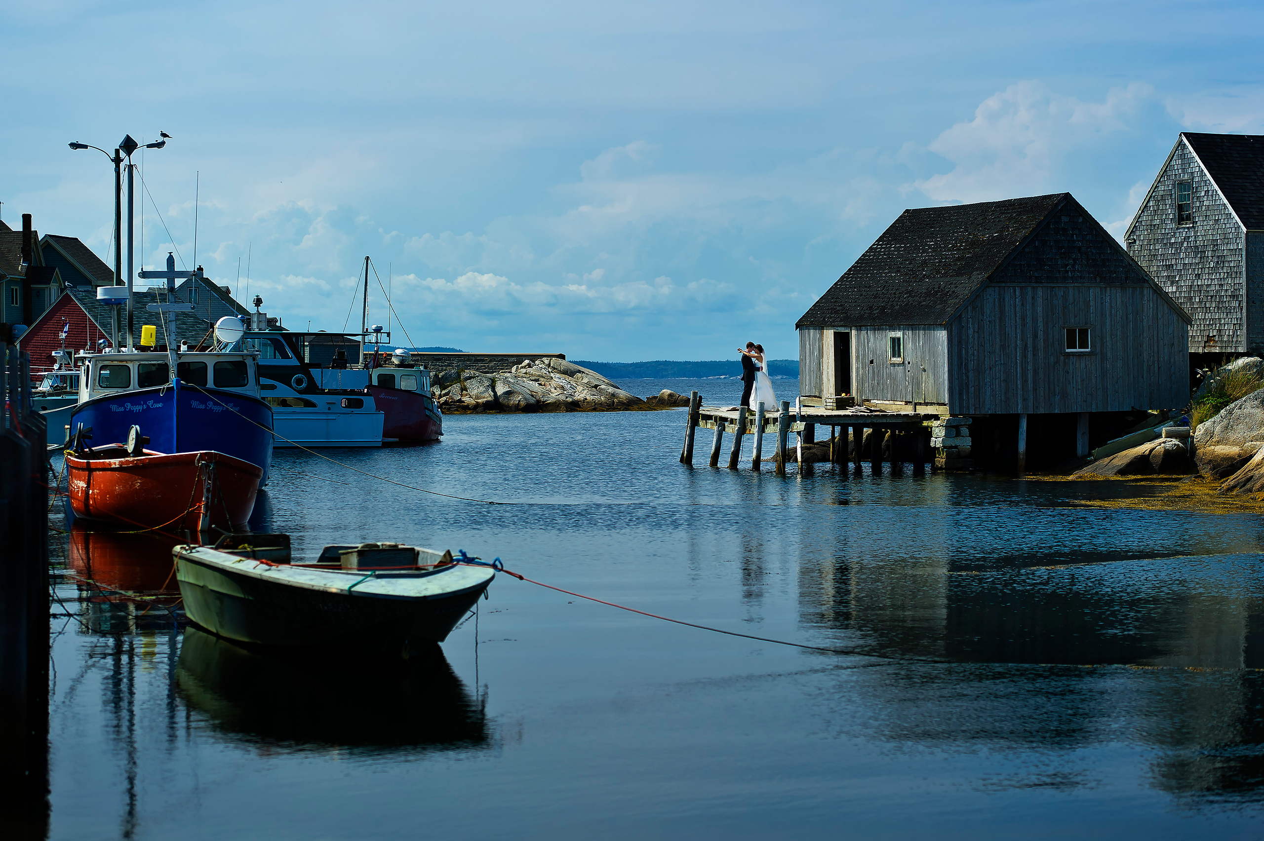 Bride and groom on a fishing wharf at Peggy's Cove with lobster boats in the harbour, Nova Scotia wedding