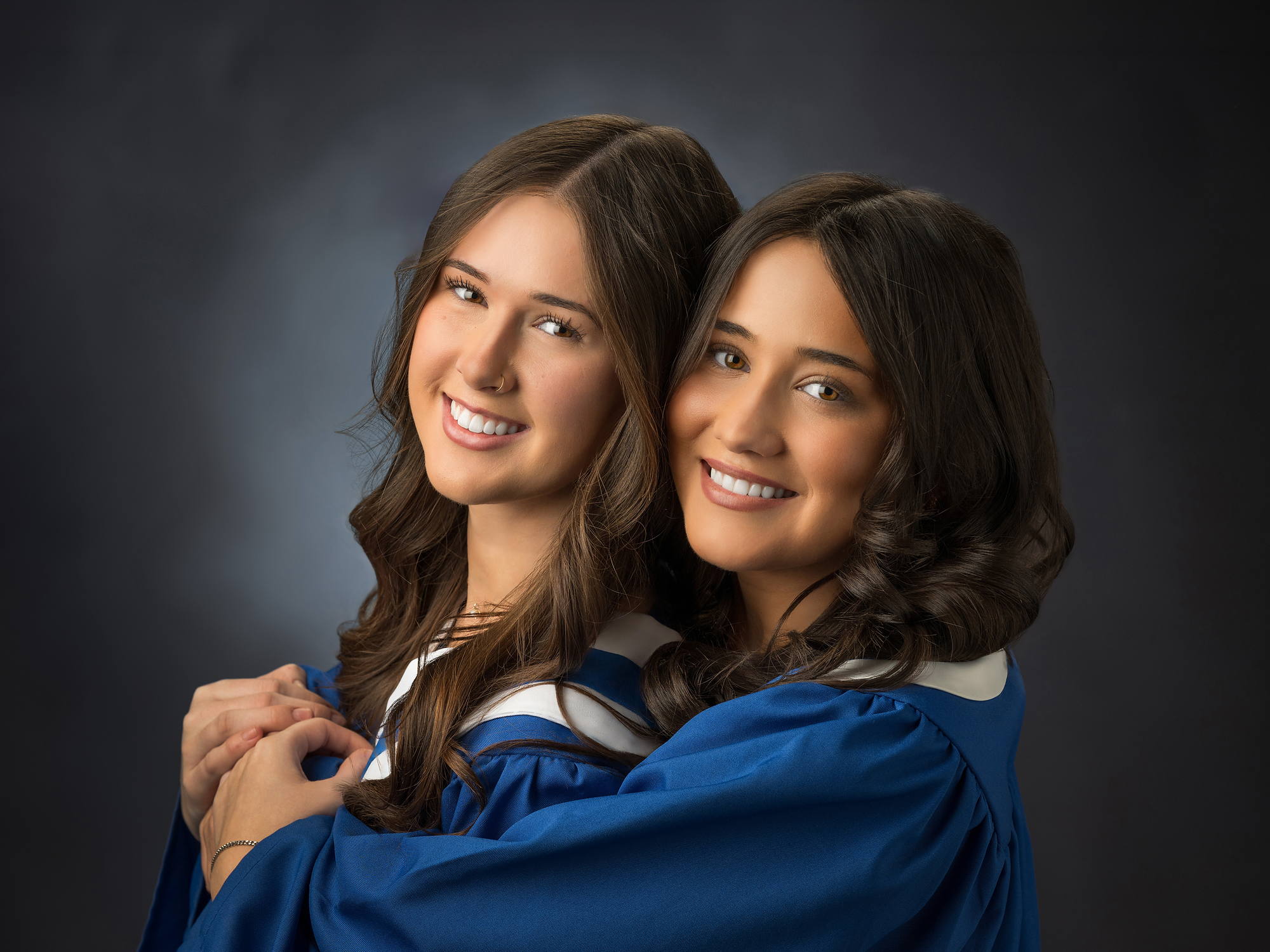 Two grads in blue gowns hugging in the studio, Grad Plus session in Halifax