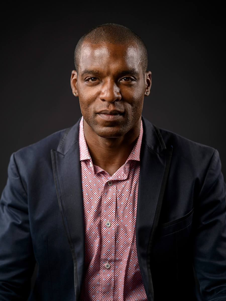CEO headshot of JT Manning in a navy blazer and checked shirt on a dark grey background, Halifax