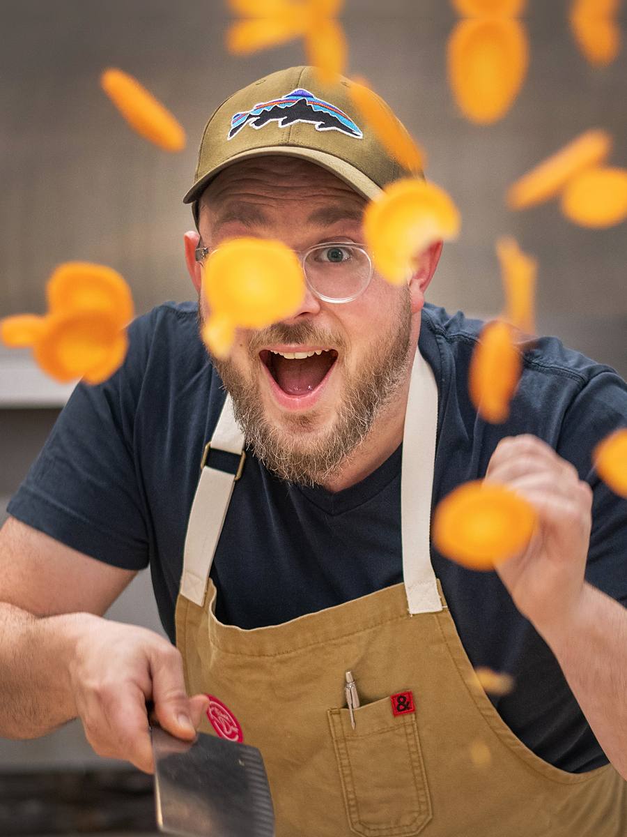 Chef Andrew Farrell of Kitchen Door Catering laughing as he tosses sliced carrots in the kitchen, Dartmouth