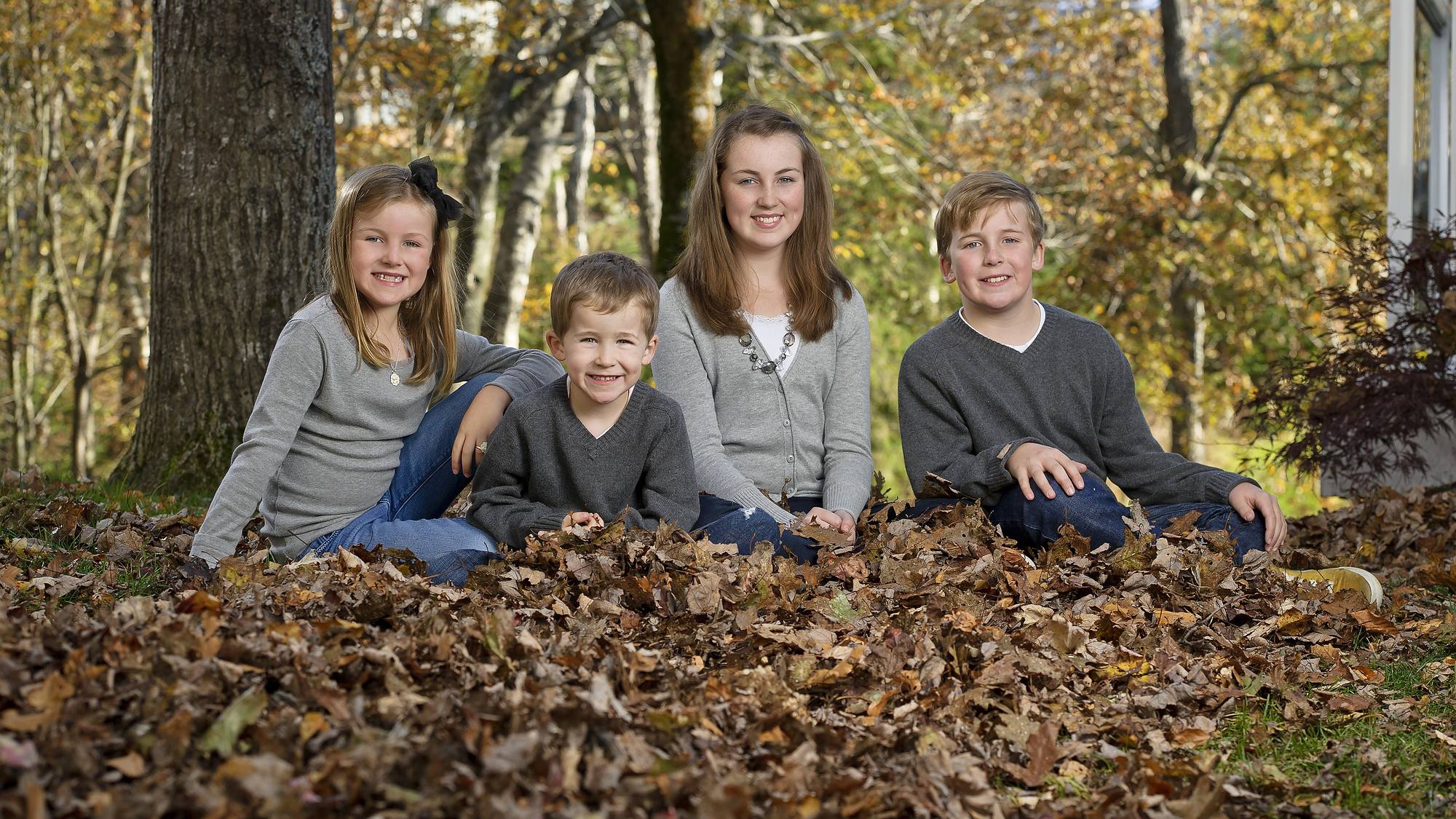 Family of four sitting in deep autumn leaves - fall family session in Bedford, Nova Scotia
