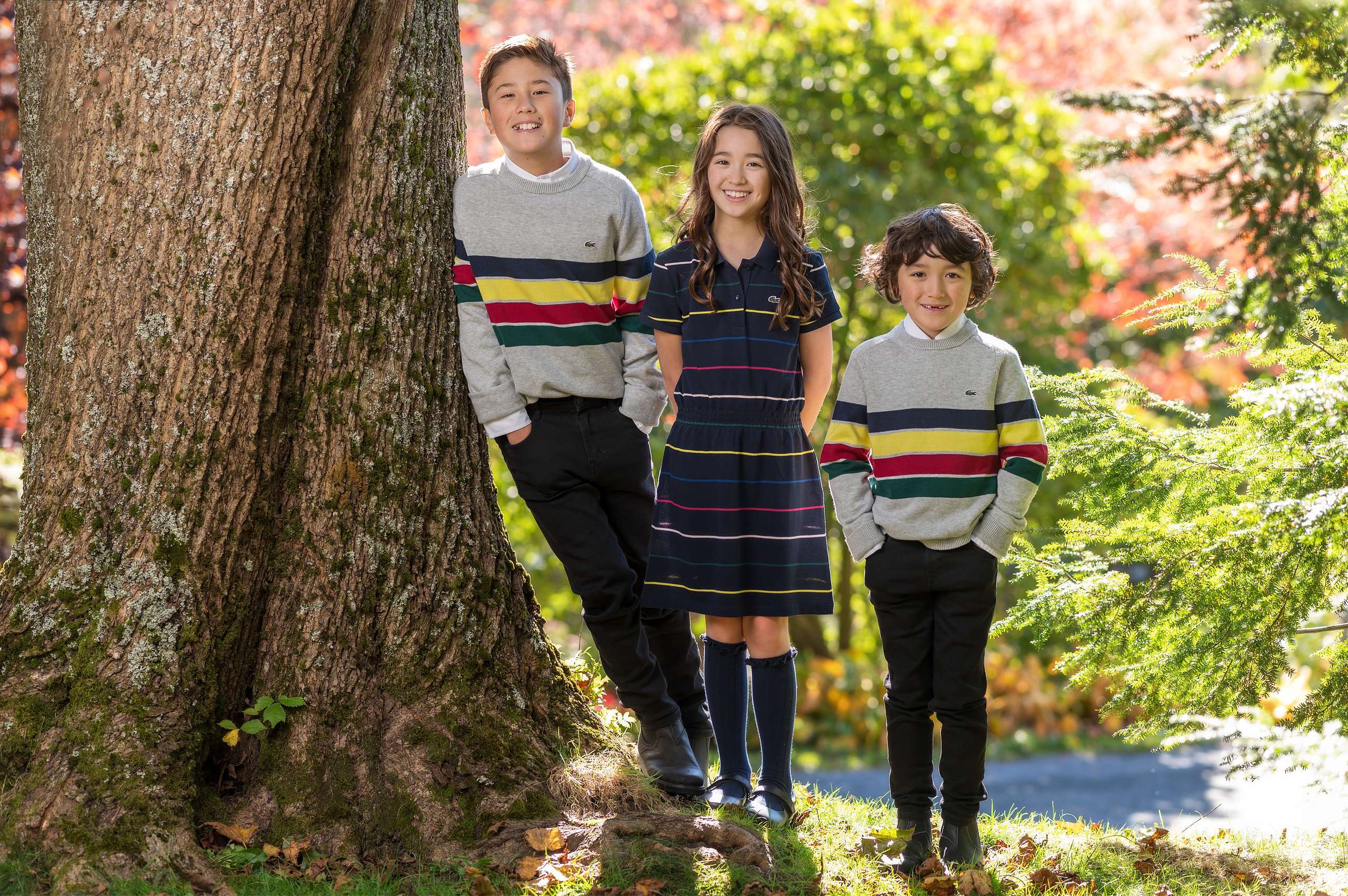 Three kids in striped sweaters beside a big maple in red fall colour - autumn family session in Nova Scotia
