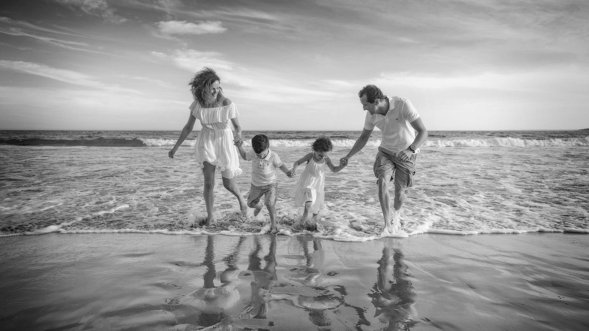 Black and white photo of a family of four running through the surf on a Nova Scotia beach