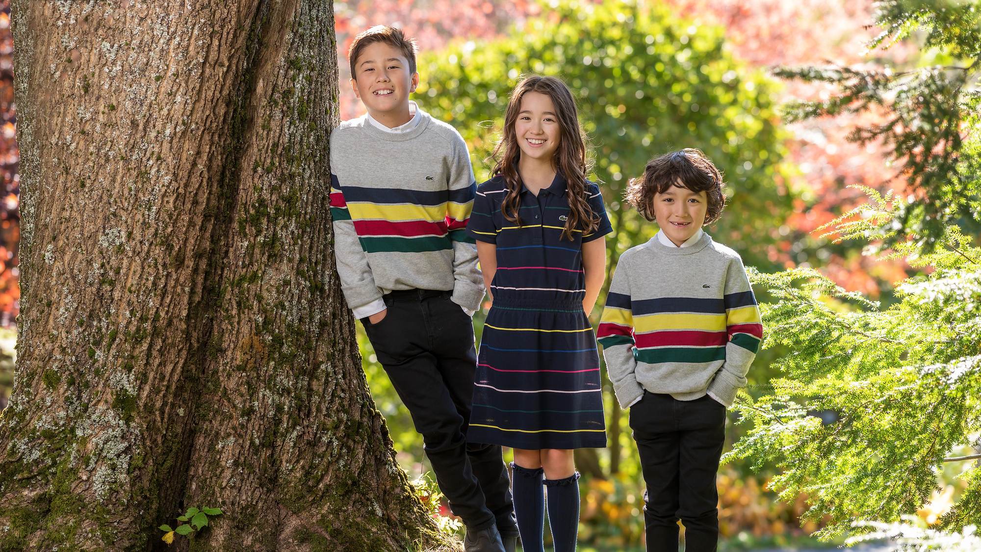 Three kids in striped sweaters beside a big maple in red fall colour - autumn family session in Nova Scotia