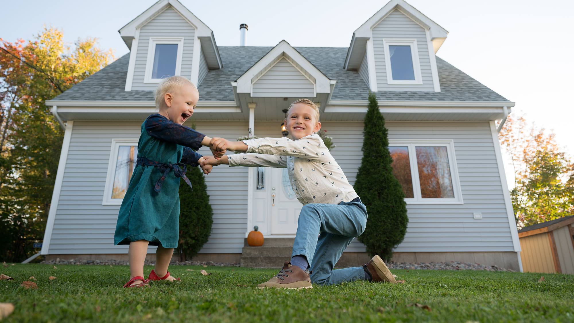 Two kids swinging hands in front of their home with a pumpkin on the step - fall family session