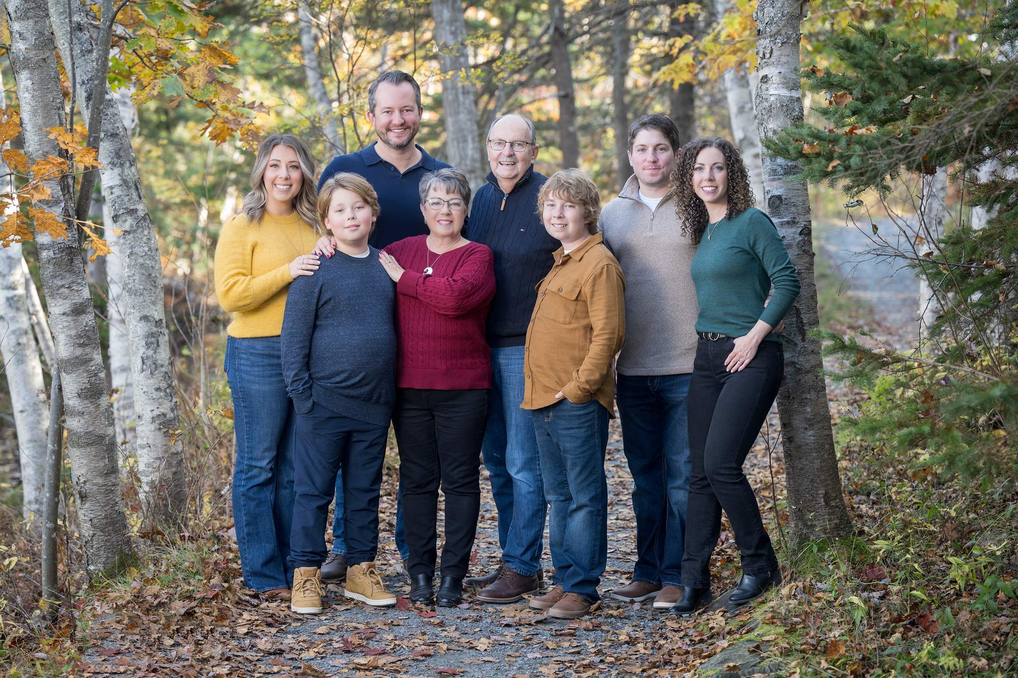 Extended family of eight standing together on a birch-lined trail in fall colours, Nova Scotia family photos