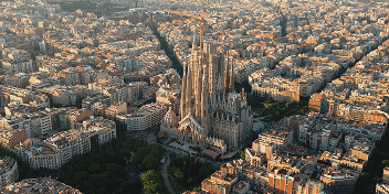 Aerial view of the Sagrada Família basilica surrounded by buildings in Barcelona at sunset.