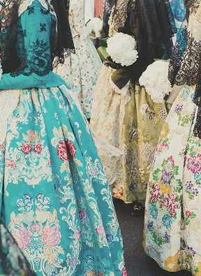 Women wearing colorful traditional dresses with floral patterns holding white flower bouquets.