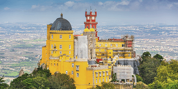 Colorful Pena Palace with red and yellow towers atop a green hillside under a blue sky.