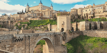 Historic stone bridge and medieval city walls under blue sky in Toledo, Spain.