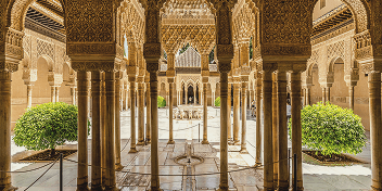 Ornate arches and columns in a historic Andalusian courtyard with symmetrical green bushes.
