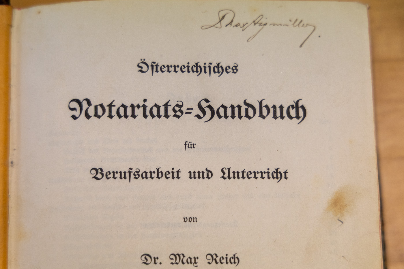 Nahaufnahme einer historischen Titelseite des 'Österreichischen Notariats-Handbuchs' von Dr. Max Reich in Frakturschrift mit handschriftlicher Signatur am oberen Rand.