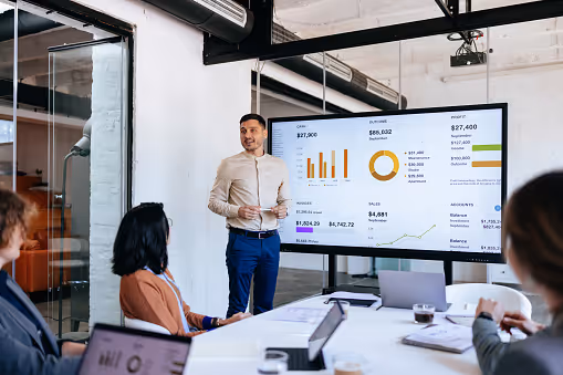 Man presenting financial data on screen to colleagues seated at conference table.