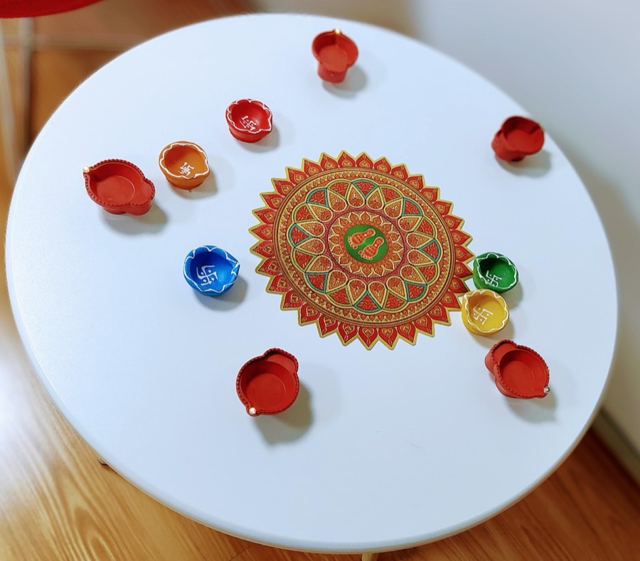 Hand-painted clay diyas arranged in a ring around a printed rangoli on a white table