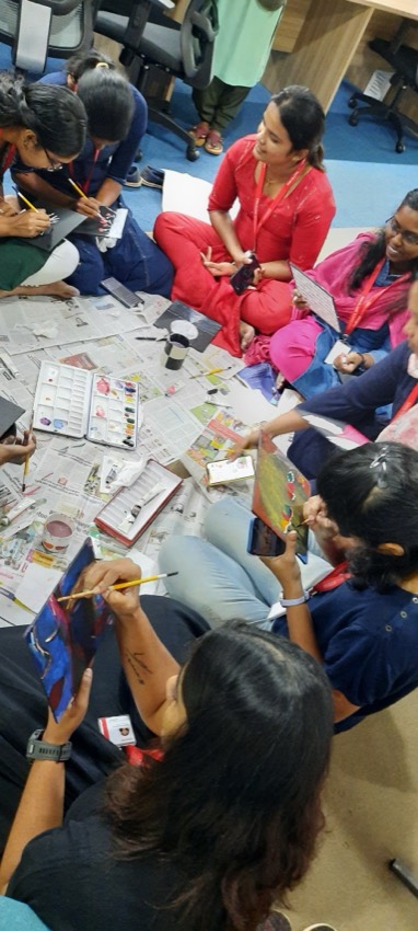 Colleagues seated around a table painting on small canvases with acrylic paints
