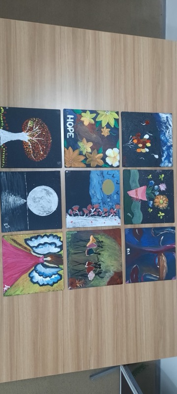 Nine finished paintings laid out in a grid on a wooden desk, one of them titled Hope