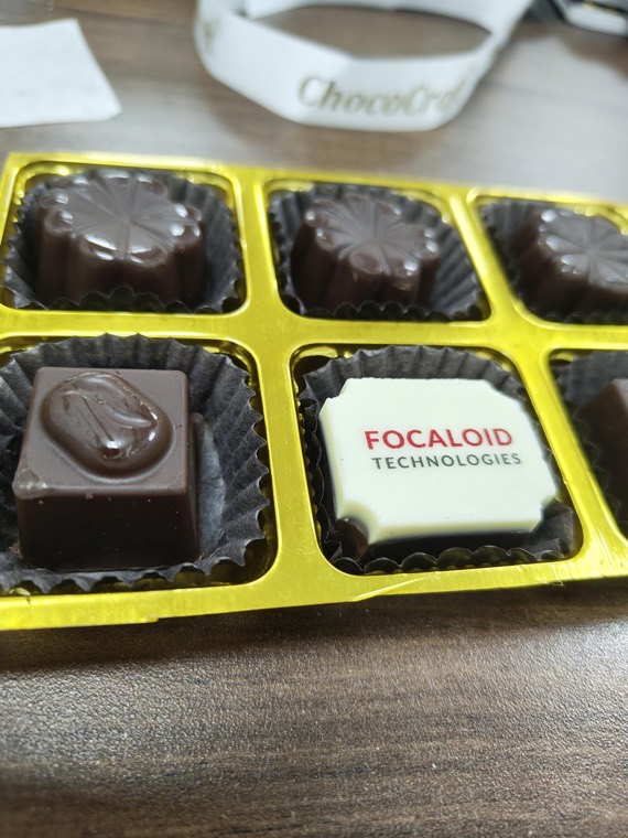 An open box of chocolates, one of them moulded with the Focaloid Technologies logo