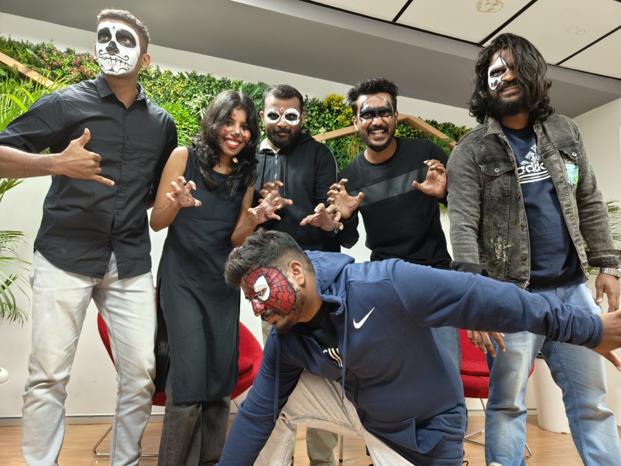 Six colleagues in skull face paint posing in front of a green plant wall