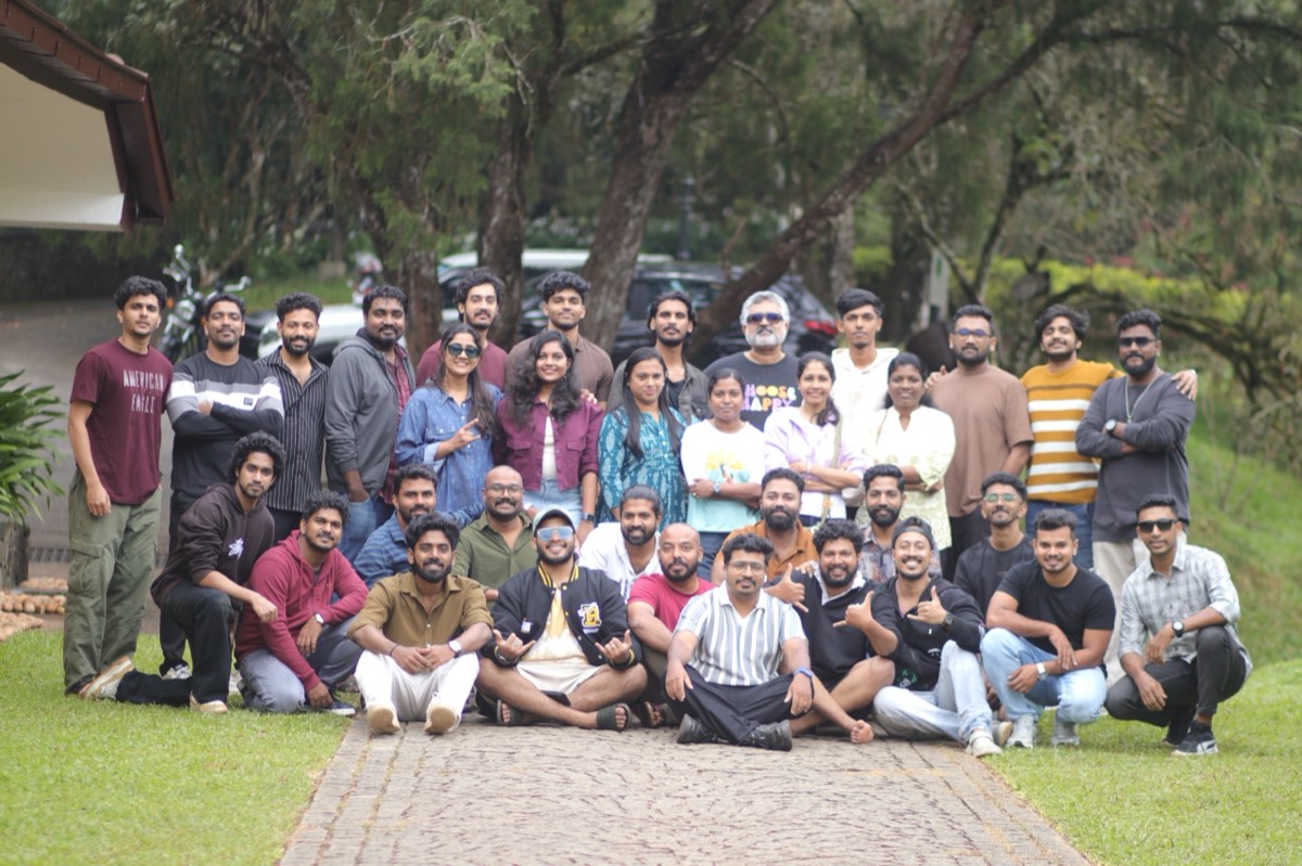 A large group of colleagues posing on a lawn among trees during a team offsite