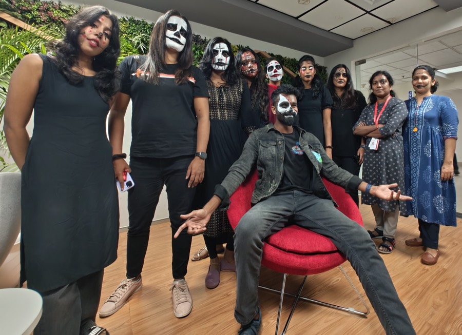 Colleagues in Halloween make-up standing around a colleague seated on a red chair