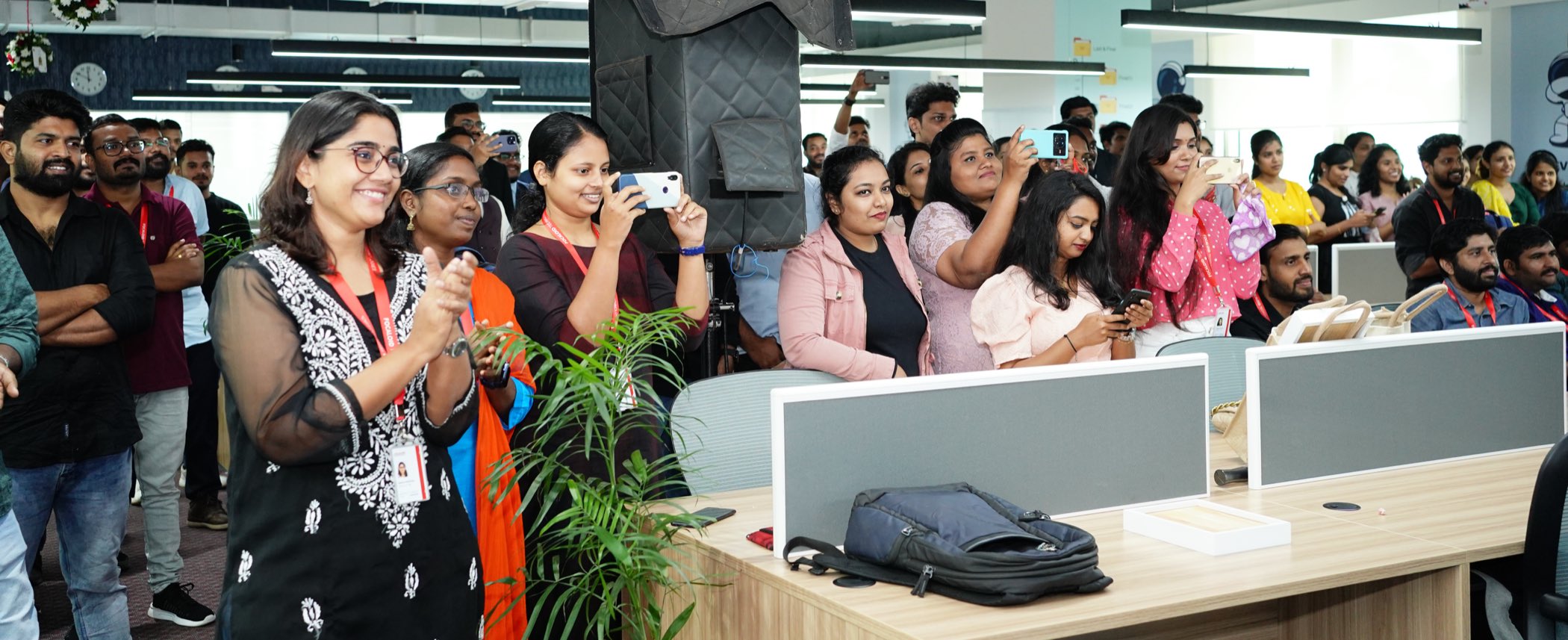 The Focaloid floor at World Trade Center Kochi: a crowd of employees standing between the desks, clapping and filming
